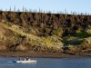 A small boat navigates shallow water below ice wedges and baydzerakhs (mounds of thawing Pleistocene permafrost soils) at the riverbank exposure of Duvannyi Yar on the Kolyma River in the Siberian Arctic.